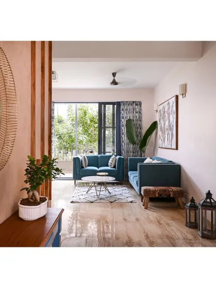 The journey into this home begins in the foyer, with a view into the living area where blue sofas and lush plants create a welcoming, colorful space.
