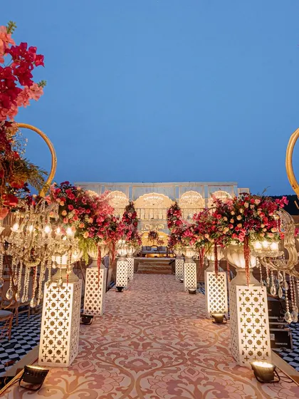 The grand aisle, lined with floral arrangements on pedestals and ornate lanterns. The checkered floor adds a classic touch to the otherwise traditional Rajasthani decor.