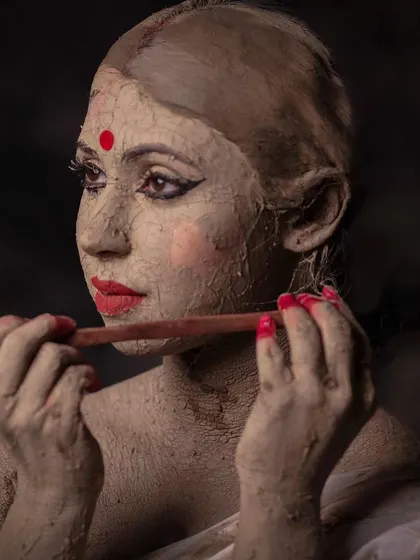 This image captures a moment of quiet grace amidst the sculpting process. The 'bele maati' or fine clay application gives the idol its smooth finish, a metaphor for the constructed nature of perfection.