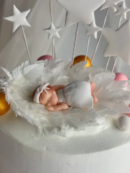 The delicate, handcrafted fondant baby topper, nestled in a bed of wafer paper feathers.