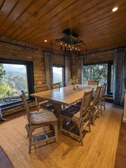 A full view of the dining room, showcasing the long wooden table perfect for family meals, the industrial-style chandelier, and the incredible mountain views from every window.