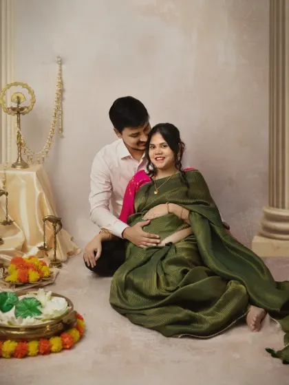 A sweet seated portrait of the couple. The husband's protective embrace and their shared smiles create a feeling of warmth and togetherness, surrounded by traditional decor.