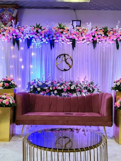 This elegant reception stage features a soft, romantic aesthetic. A floral arch of pink and white roses sits above a backdrop of white curtains and subtle lighting, with a custom monogram adding a personal touch for the couple.