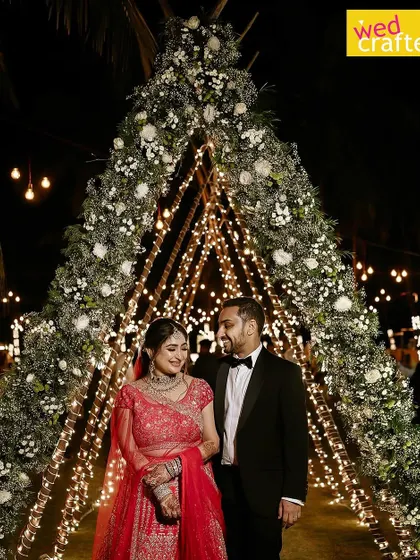 A beautiful moment captured as the couple walks hand-in-hand under the glowing floral arch. The bride's red lehenga stands out beautifully against the magical, starlit decor.