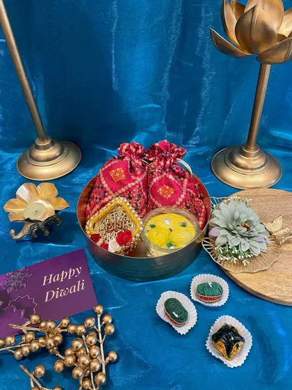 A traditional yet elegant Diwali gift set in a brass bowl. This hamper includes decorative potlis, a floating candle, and beautifully crafted sweets, perfect for festive greetings.