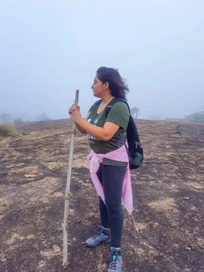 A trekker pauses with a walking stick, looking out into the foggy landscape of Bananthimari. These moments of solitude are just as important as group activities.