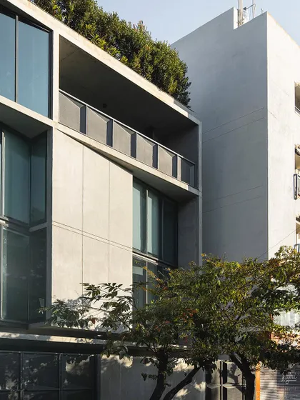 A detail of the facade of our studio, showing the relationship between the concrete structure, large glass panels, and the rooftop greenery. The building is designed to be an active participant in its street context.