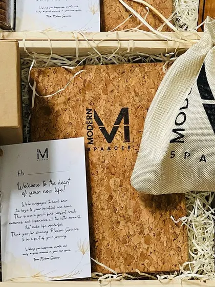 A close-up of the contents of a 'Modern Spaaces' welcome kit, including a branded cork notebook, cookie jar, and a personalized note.
