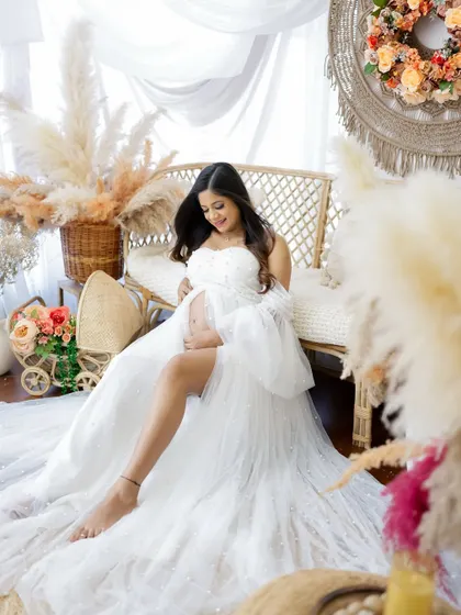 A joyful and radiant portrait in a boho-chic setting. The mom-to-be is all smiles in a beautiful white gown, surrounded by pampas grass.