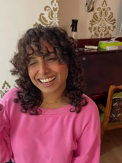 A happy client enjoying her new low-maintenance curly hairstyle.