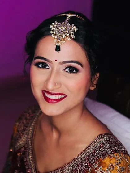 A ring-light portrait showcasing the flawless finish of the makeup. The sharp winged liner, golden eyeshadow, and bright red lip are classic bridal elements.