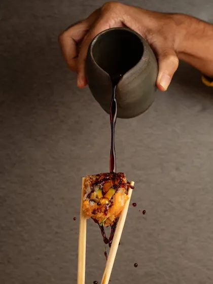 An action shot of soy sauce being poured over a piece of sushi. This dynamic image freezes a moment of flavor, making the dish look more interactive and delicious.