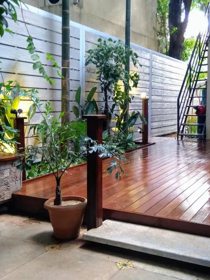 This backyard design features a raised wooden deck surrounded by lush greenery and subtle lighting, creating a tranquil and private retreat.