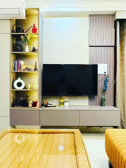 This TV unit in a Jasola home combines open and closed storage. The open shelves are backlit to highlight decorative items, while the cabinets keep clutter hidden.
