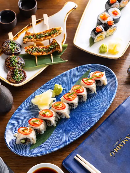 A spread of Japanese appetizers, including sushi and yakitori skewers. The composition is designed to look like a real dining table, creating a relatable scene.