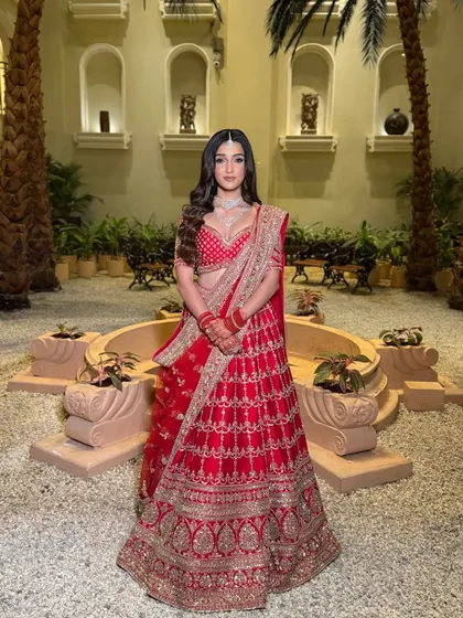 A regal portrait. The bride stands in a beautiful courtyard, her red lehenga and diamond jewellery complemented by a makeup look that is both classic and contemporary.