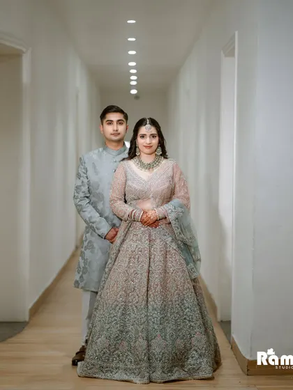 A full-length portrait of the couple in a modern, well-lit corridor. Their coordinated pastel outfits look elegant and sophisticated.