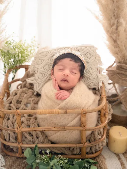 A peaceful portrait from a boho session, with the baby swaddled in a neutral wrap and resting in a natural fiber basket surrounded by pampas grass.