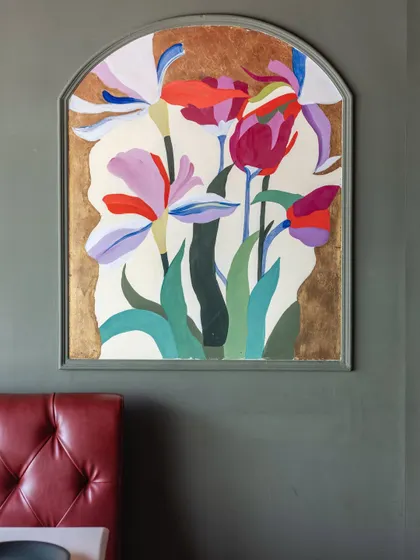 A finished view of an arched floral panel in a restaurant, featuring stylized irises and tulips against a gold leaf background. The artwork adds a touch of elegance and color to the dining space.