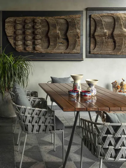 The family lounge opens onto a serene terrace with an outdoor dining area. The wall features antique carved wooden panels, adding a layer of history and texture to the space.