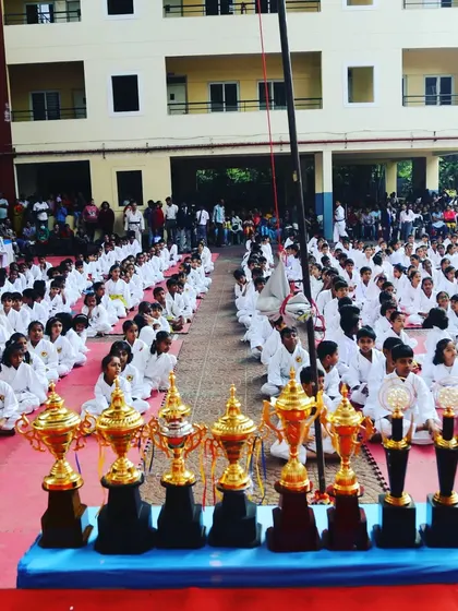 Trophies in the foreground with rows of disciplined students behind them. This image symbolizes the goal and the journey of every competitor at our championships.