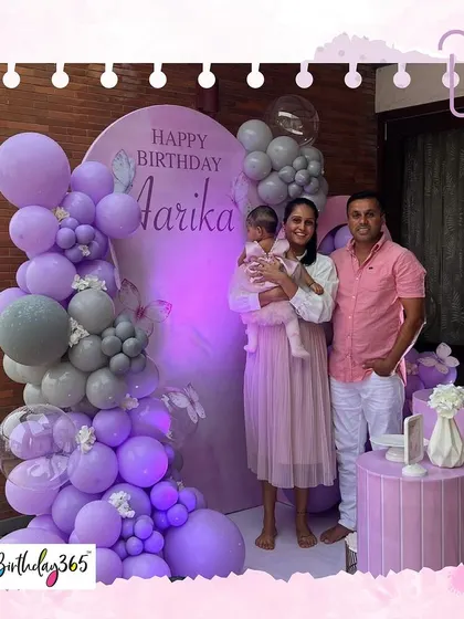 The happy family celebrating Aarika's first birthday, posing in front of the custom butterfly-themed backdrop we designed.