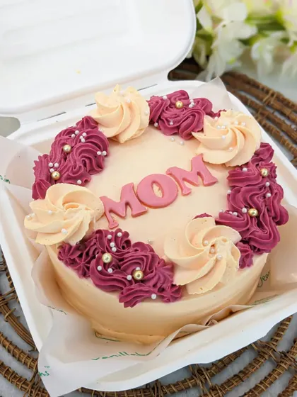 A close-up of our "MOM" bento cake, decorated with delicate buttercream swirls in two tones and sprinkled with edible pearls. It's a beautiful and delicious way to celebrate her.