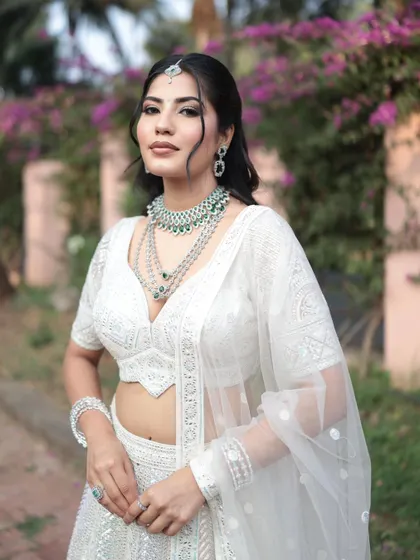 A beautiful portrait in the white lehenga, with a focus on the layered diamond and emerald necklace set. The soft makeup complements the elegant attire.