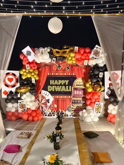 A full view of a terrace Diwali party setup with a 'Happy Diwali' backdrop, casino-themed balloon arch, and floor seating.