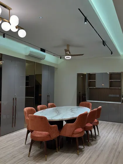 This dining room combines bold color with sleek design. A marble-topped oval dining table is surrounded by plush orange chairs, set against high-gloss grey cabinetry with bronze mirror accents for a modern, sophisticated look.
