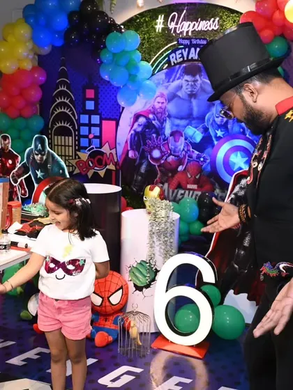 The birthday girl is doing a fantastic job assisting with a floating ball trick at her superhero themed party. It's all about empowering the kids and making them part of the magic.