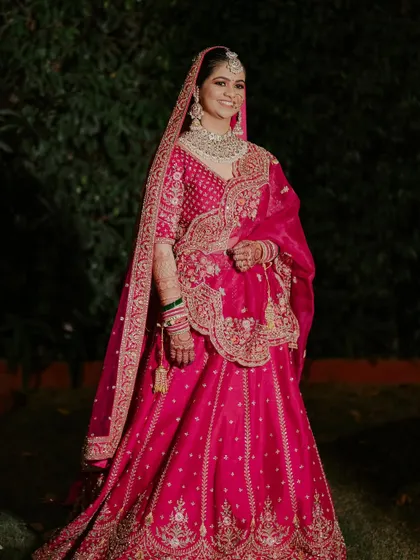 A full-length shot of the bride in her magnificent pinkish-red lehenga. The makeup is balanced perfectly to complement the heavy outfit and jewelry.