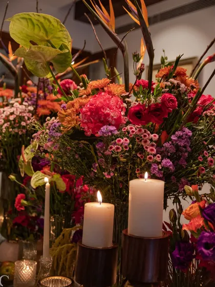 A close-up of the vibrant floral arrangements, with the soft glow of candles highlighting the rich pinks, oranges, and purples. This image captures the warmth and energy of the design.