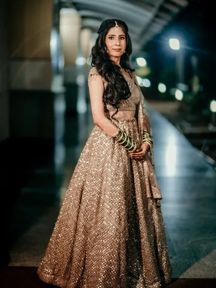 A full-length shot of the bride in her glittering gold lehenga. The makeup is glamorous and sophisticated, balancing the sparkle of her outfit.