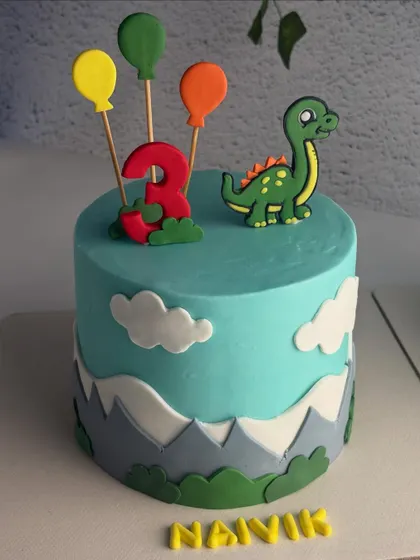 A close-up of one of the twin dinosaur cakes, showing the cute fondant dino and balloon toppers.