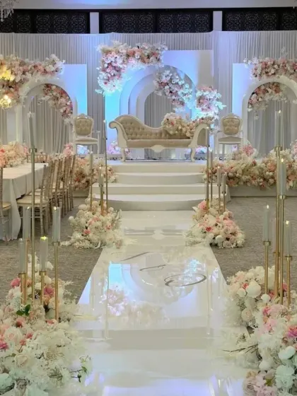An all-white and pink themed stage for a Nikkah or reception, featuring a reflective aisle and elegant floral arrangements.