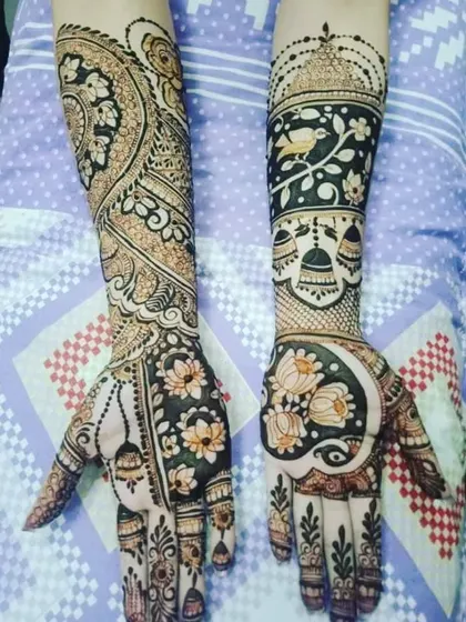 A unique and artistic design with hanging bells (jhumkas) and birds on one arm, and a large peacock and lotus on the other.