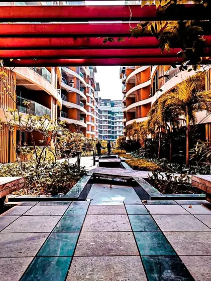 A view through a red pergola at the Palm Bellagio project in Raipur. This image highlights our landscape and amenity design, where we create inviting pathways and seating areas that complement the main architecture.