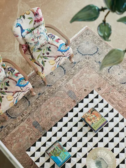 An overhead view of the living room, showing the intricate patterns of the Persian rug and the geometric black and white coffee table. The floral armchairs add a touch of traditional elegance.