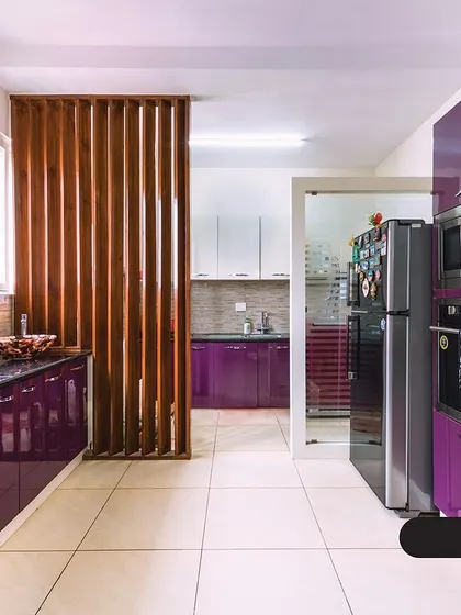 This kitchen makes a bold statement with glossy, plum-purple cabinets. The design includes a dedicated utility area separated by a wooden screen, maximizing space and organization in a stylish way.