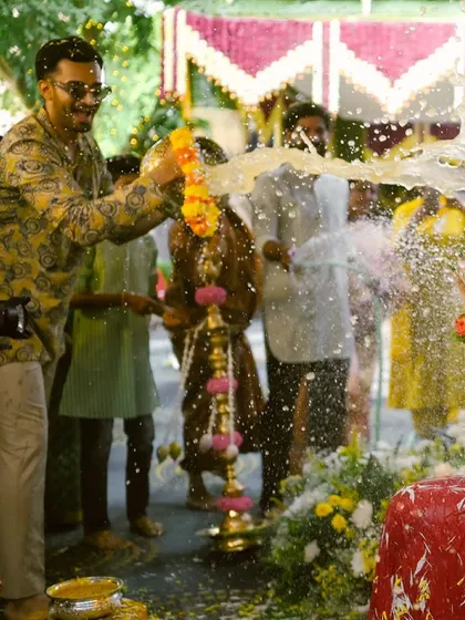 A guest playfully pours water on the groom during a pre-wedding ritual, a moment filled with laughter and fun.