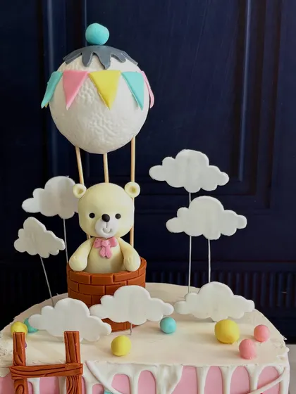A close-up of the adorable teddy bear in a hot air balloon topper from Mira's "Half Way to One" cake.