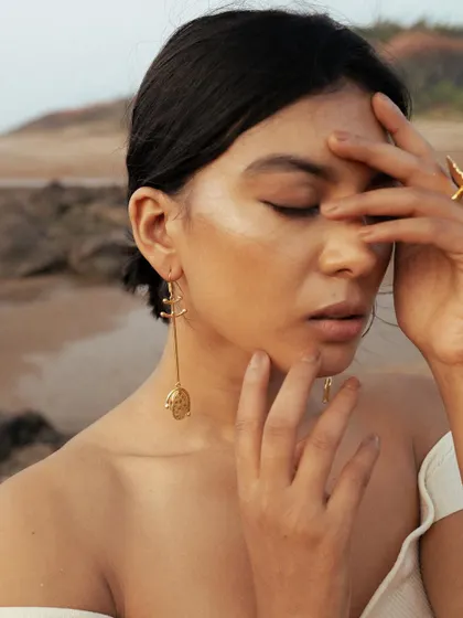 A close-up from the beachside jewellery shoot. The focus is on the glowing, highlighted skin and the simple, messy bun, which allows the statement earrings to stand out.