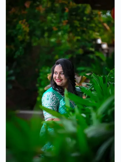 A candid shot of the bride-to-be, framed by lush greenery during her outdoor engagement party.