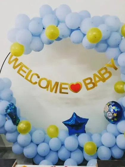 A simple and sweet "Welcome Baby" decoration. The ring of light blue balloons with yellow accents and a gold foil banner is perfect for a home celebration.