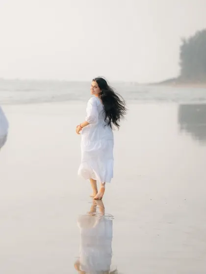 A candid shot of the bride-to-be running playfully on the beach, looking back with a smile. Her hair is caught in the wind, creating a sense of freedom and happiness.