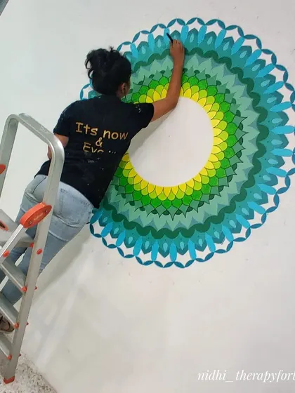On a ladder, meticulously painting the outer layers of the large mandala. This kind of detailed work at height requires both a steady hand and strong focus.