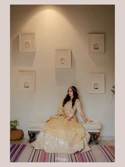 A wide portrait of the bride, showcasing her on a bench against a minimalist, chic wall.