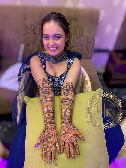 A happy bride with her beautifully detailed full-arm mehandi. The design features elephants and traditional architecture, creating a royal and elegant look.