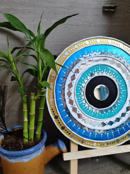 The evil eye Lippan art displayed on a wooden easel, showing how it can be used as a decorative accent on a shelf or table.